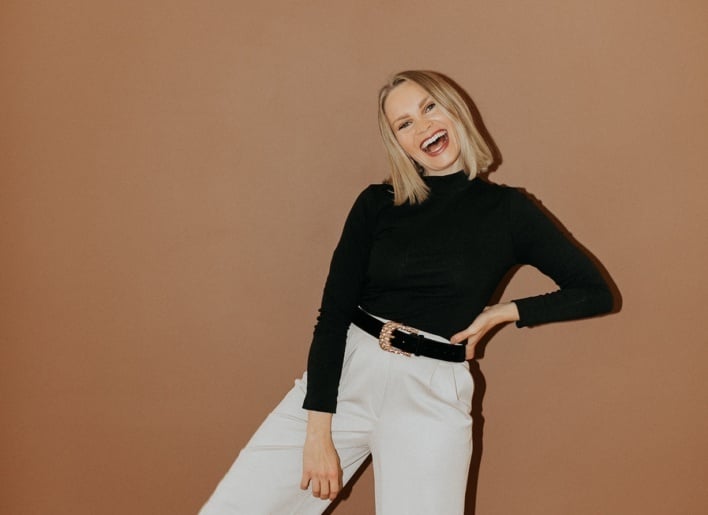 blonde woman smiling in front of a tan background