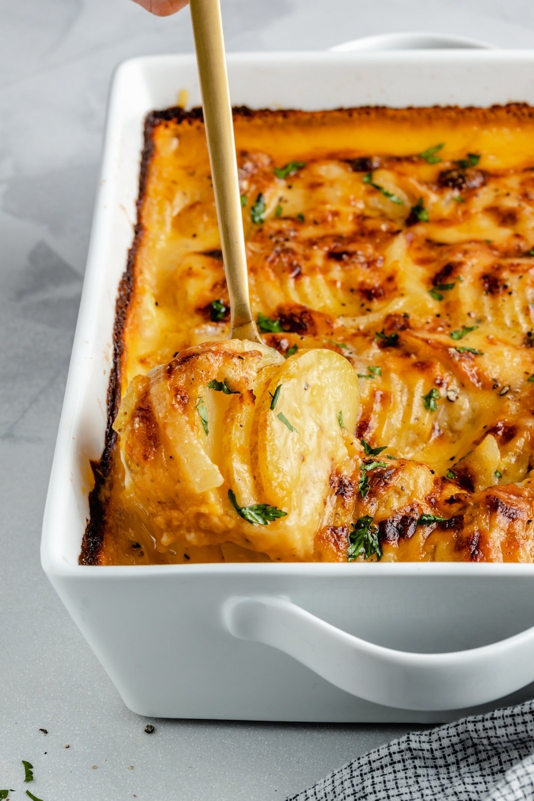 spoon lifting up a scoop of au gratin potatoes from a baking dish