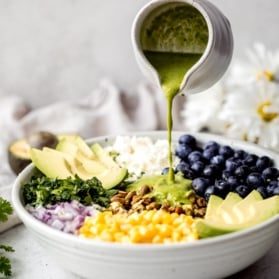 pouring homemade cilantro lime dressing onto a salad with corn, avocado, quinoa and blueberries