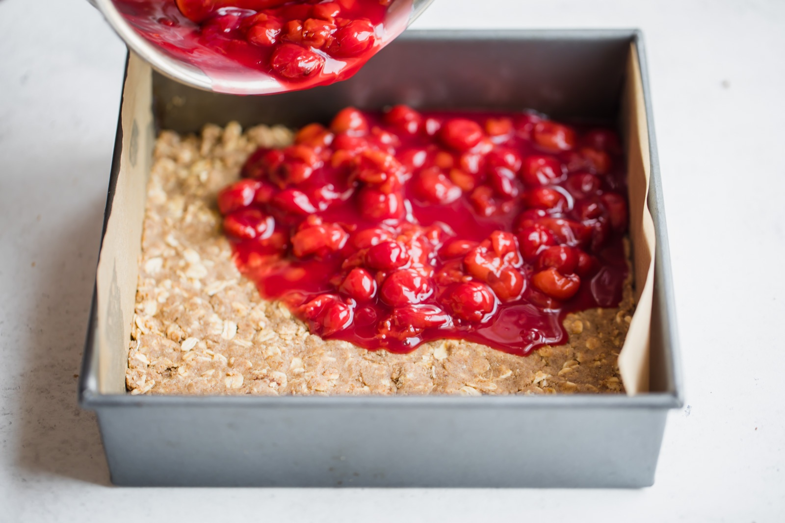 tart cherry filling being poured onto crust in a square pan