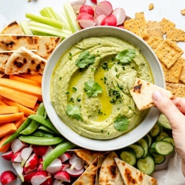 dipping pita bread into a bowl of pesto hummus