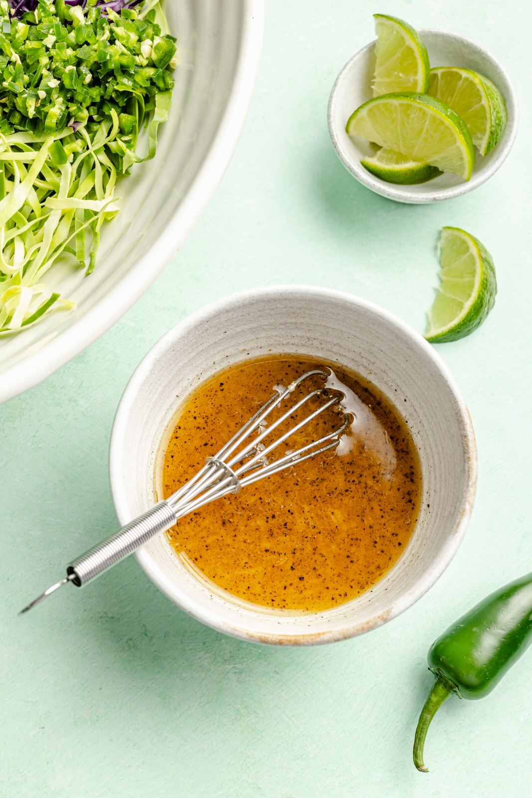 dressing for a cucumber slaw in a bowl with a small whisk