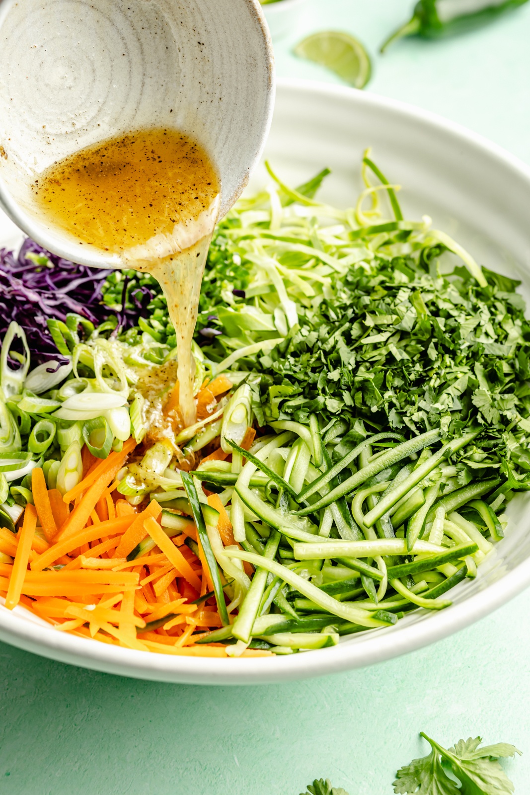 pouring dressing into a bowl of cucumber cabbage slaw