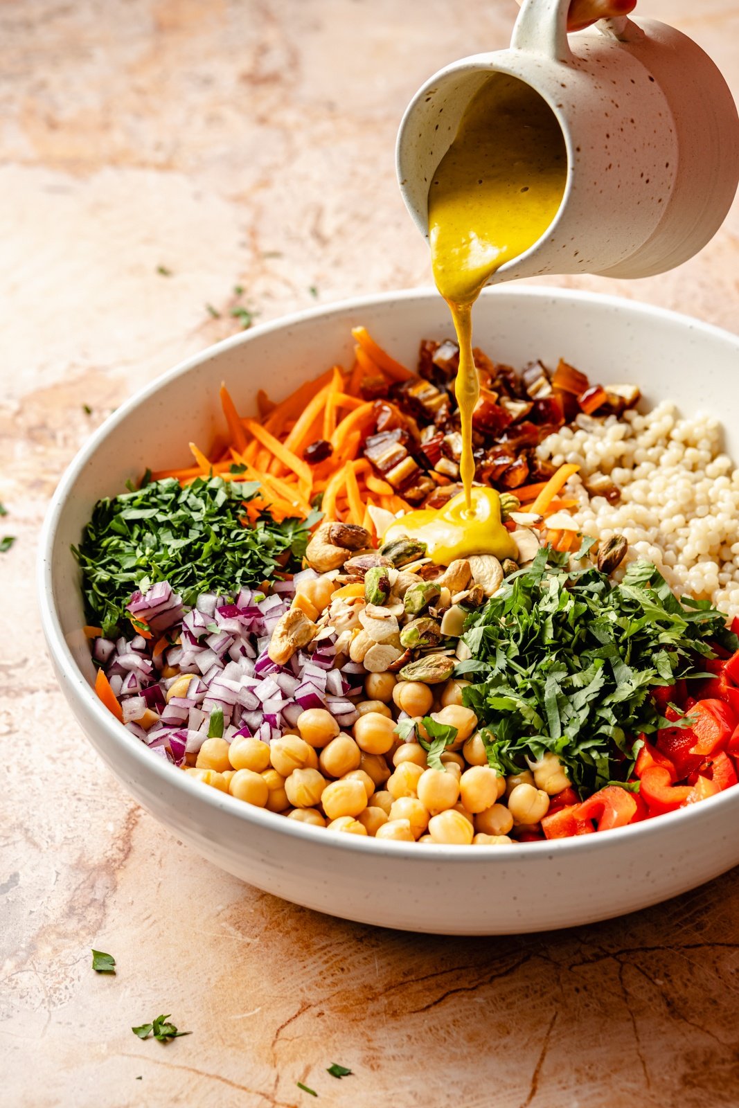 pouring dressing into a bowl with curried couscous salad