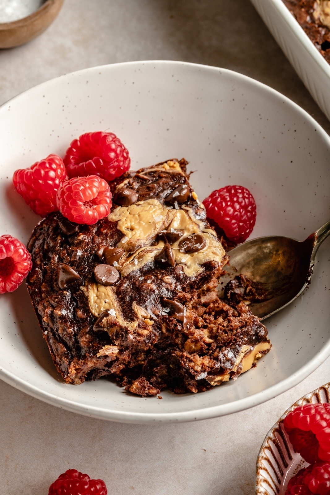 slice of chocolate peanut butter banana baked oatmeal in a bowl with raspberries