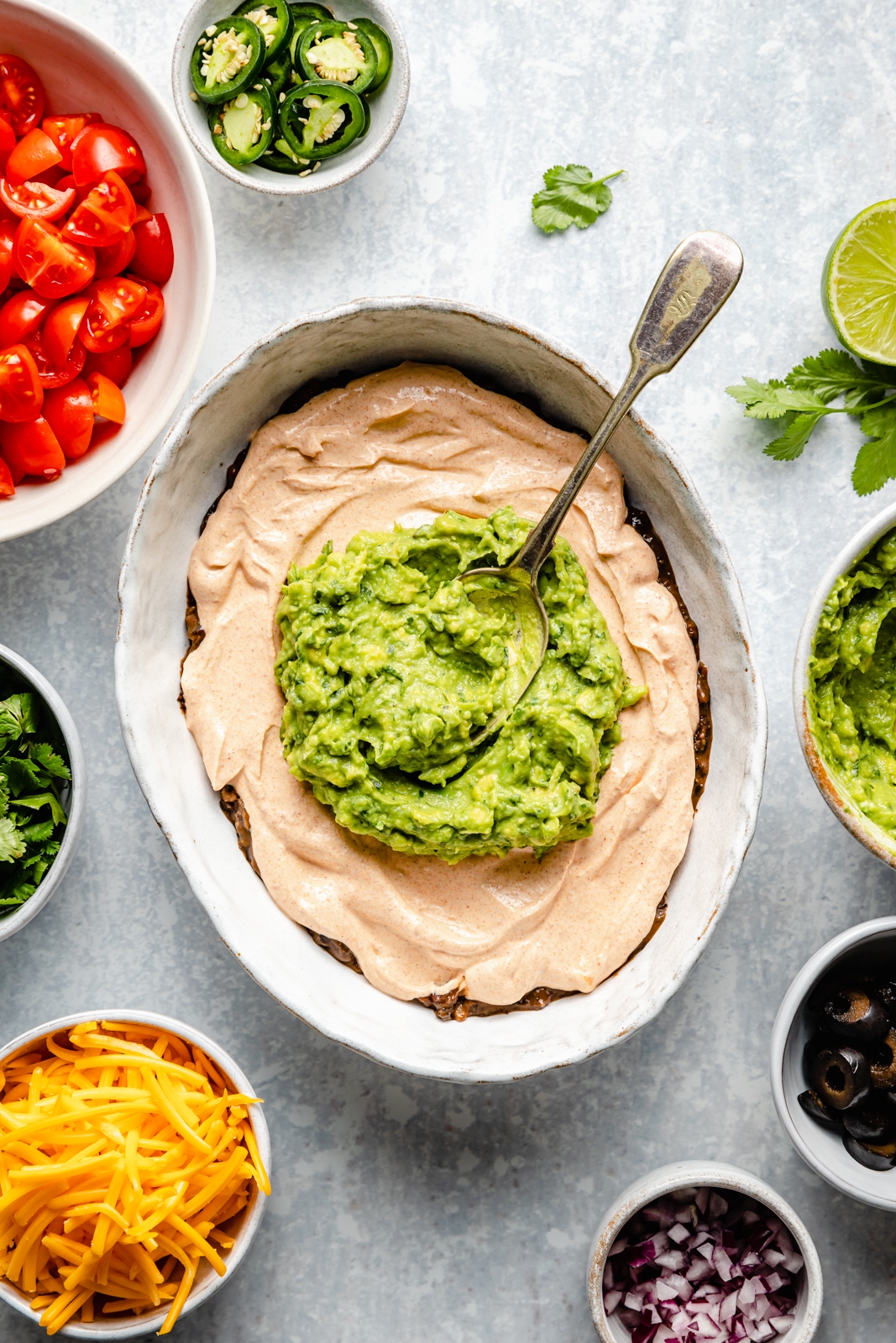 adding guacamole to healthy 7-layer dip in a serving bowl