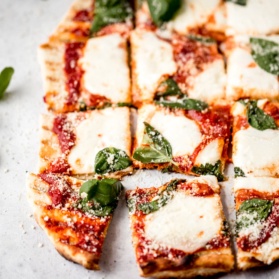 grilled pizza with cheese, tomato sauce, and basil cut into 16 squares