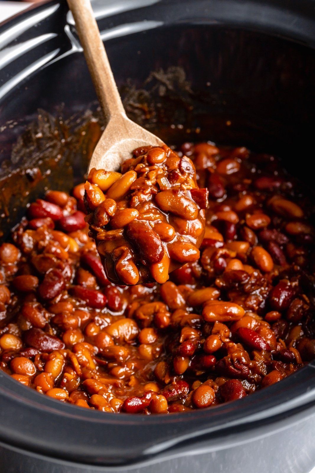 spooning up baked beans out of a slow cooker