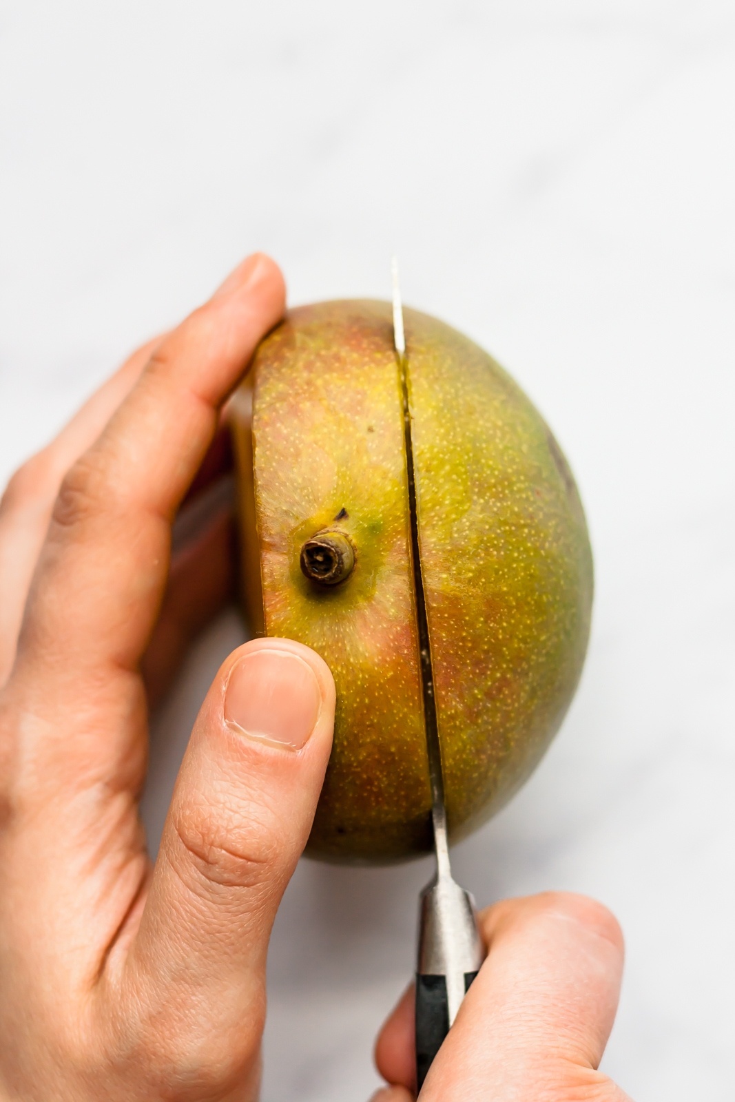 cutting half of a mango with a knife