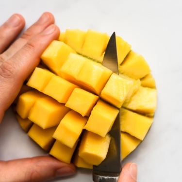 cutting mango cubes off of half of a mango