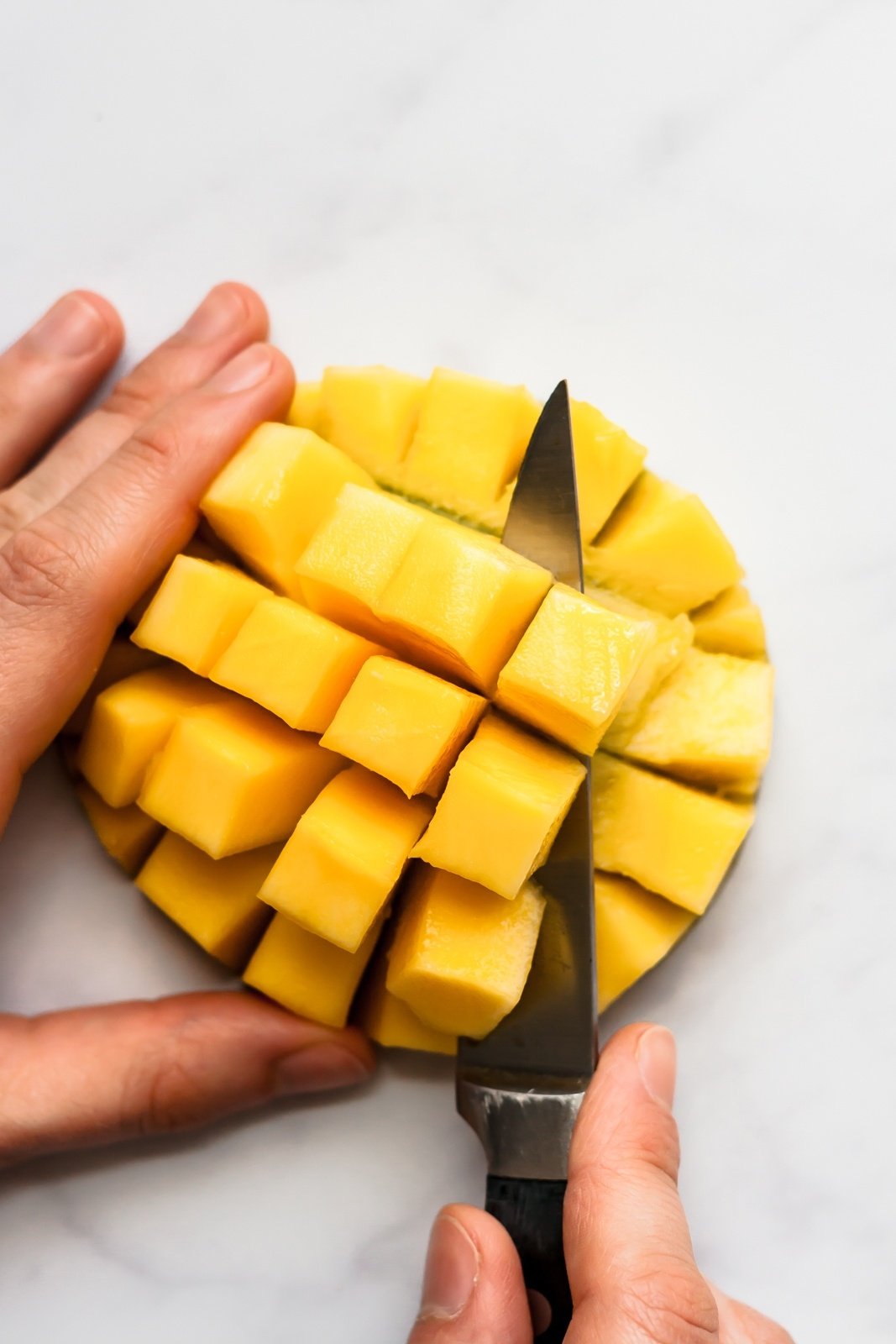 slicing mango cubes off of half of a mango