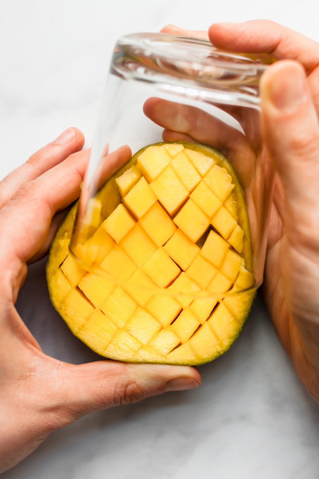 scooping mango cubes out of half of a mango with a cup