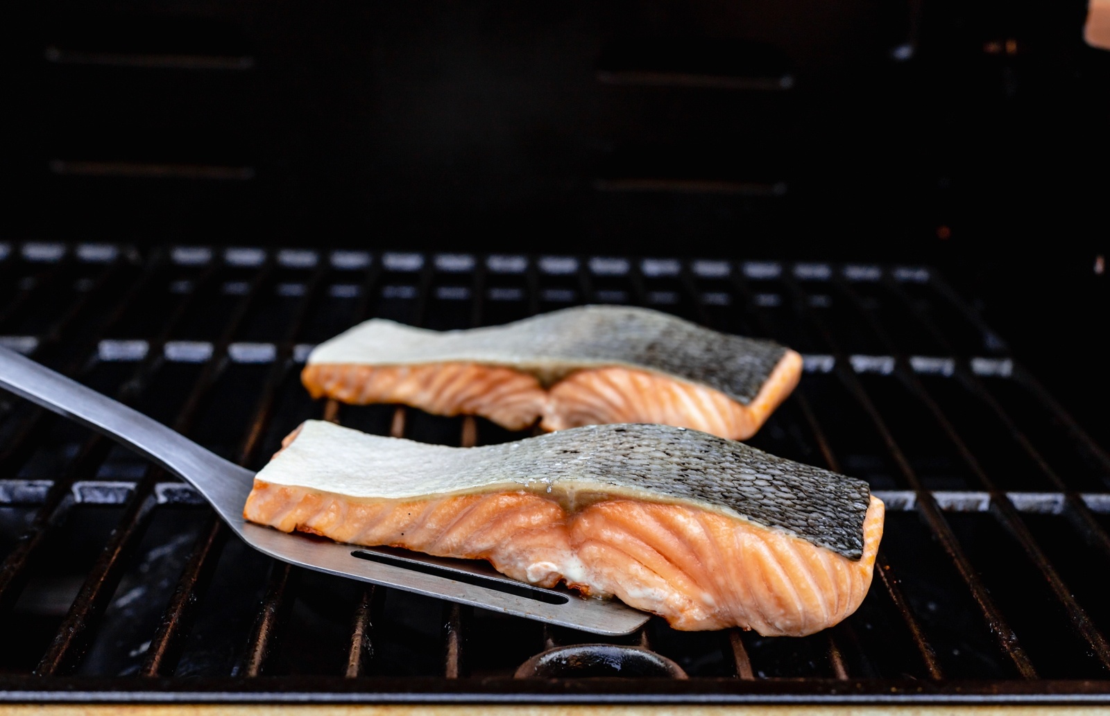 two pieces of salmon on a grill with a spatula