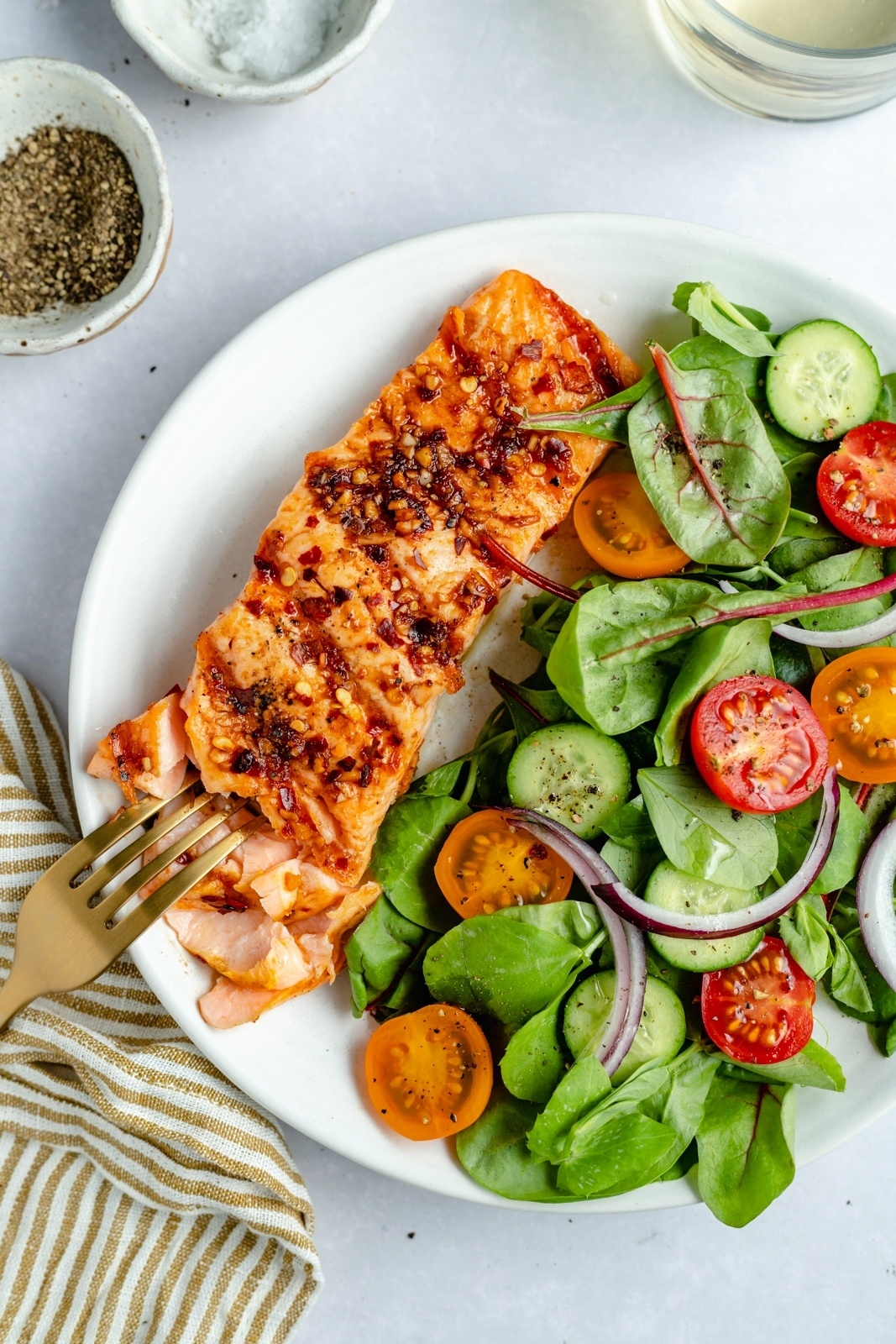 flaking grilled salmon with a fork on a plate with a side salad