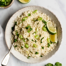 cauliflower rice in a bowl with scallions and limes