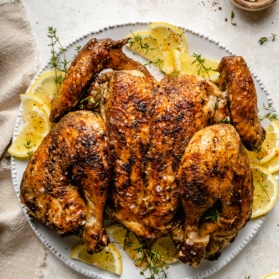 spatchcock chicken on a plate with sliced lemons