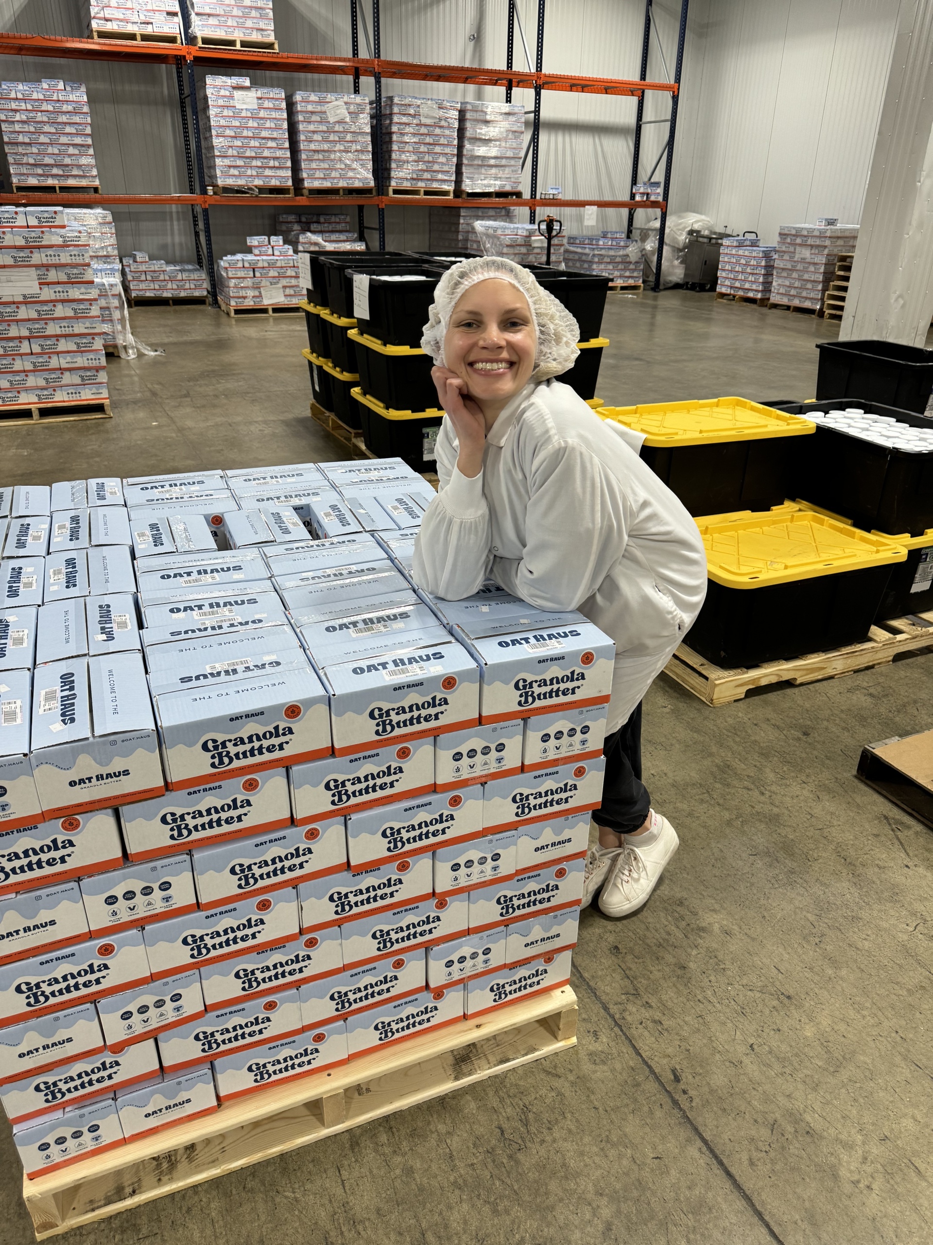 Monique Volz of Ambitious Kitchen in a factory with boxes of Cherry Pie Granola Butter