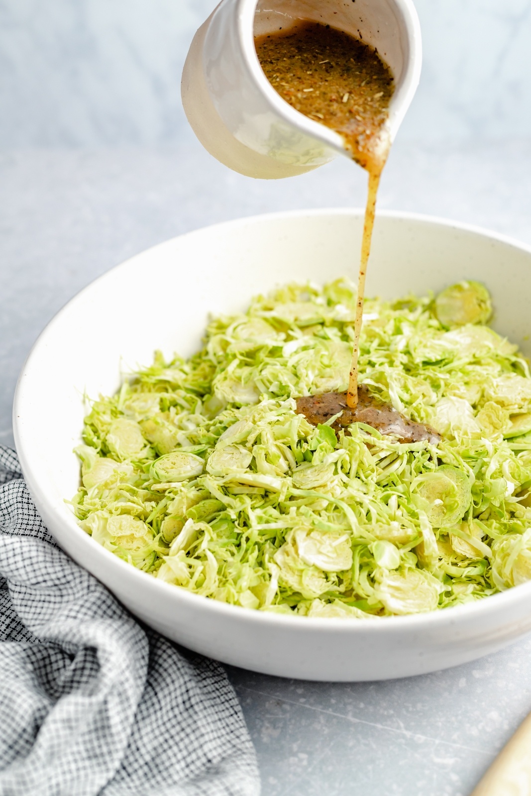 pouring italian dressing into a bowl of chopped brussels sprouts