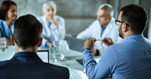 Rear view of businessmen having a business meeting with team of doctors at doctor's office.