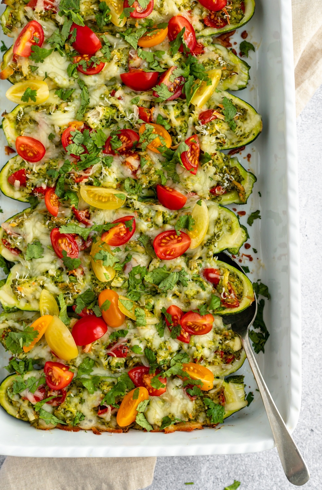 pesto chicken stuffed zucchini boats topped with tomatoes in a baking dish