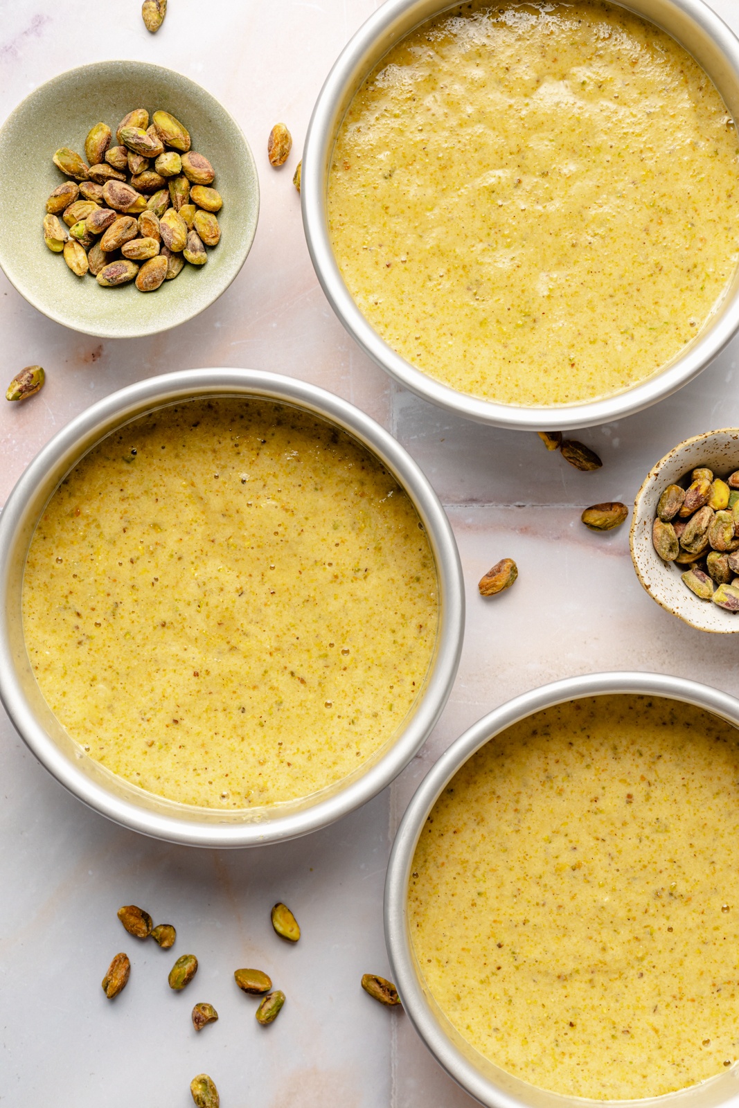 unbaked gluten free pistachio cake layers in three round cake pans