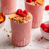 peach smoothie in glasses topped with granola and fruit