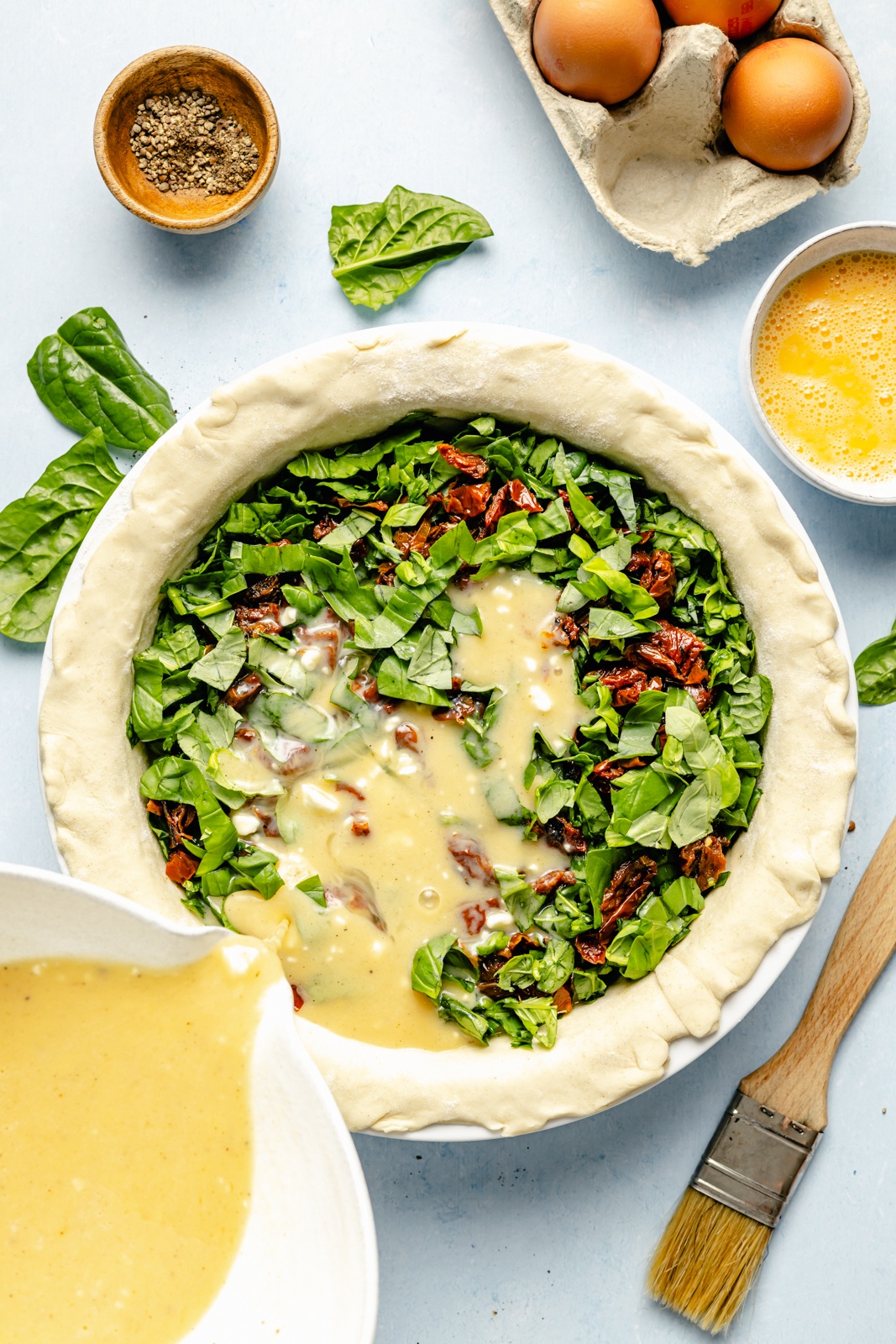 pouring an egg mixture into an unbaked spinach and sun-dried tomato puff pastry quiche