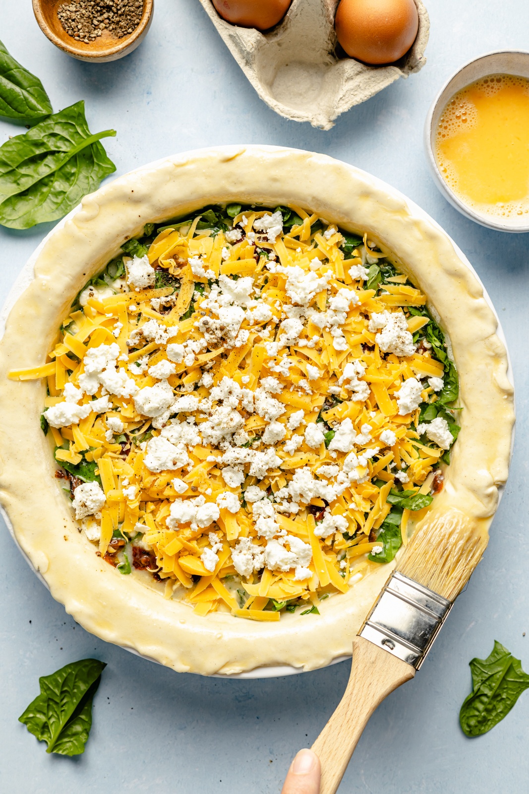 brushing an egg wash onto an unbaked sun-dried tomato basil puff pastry quiche