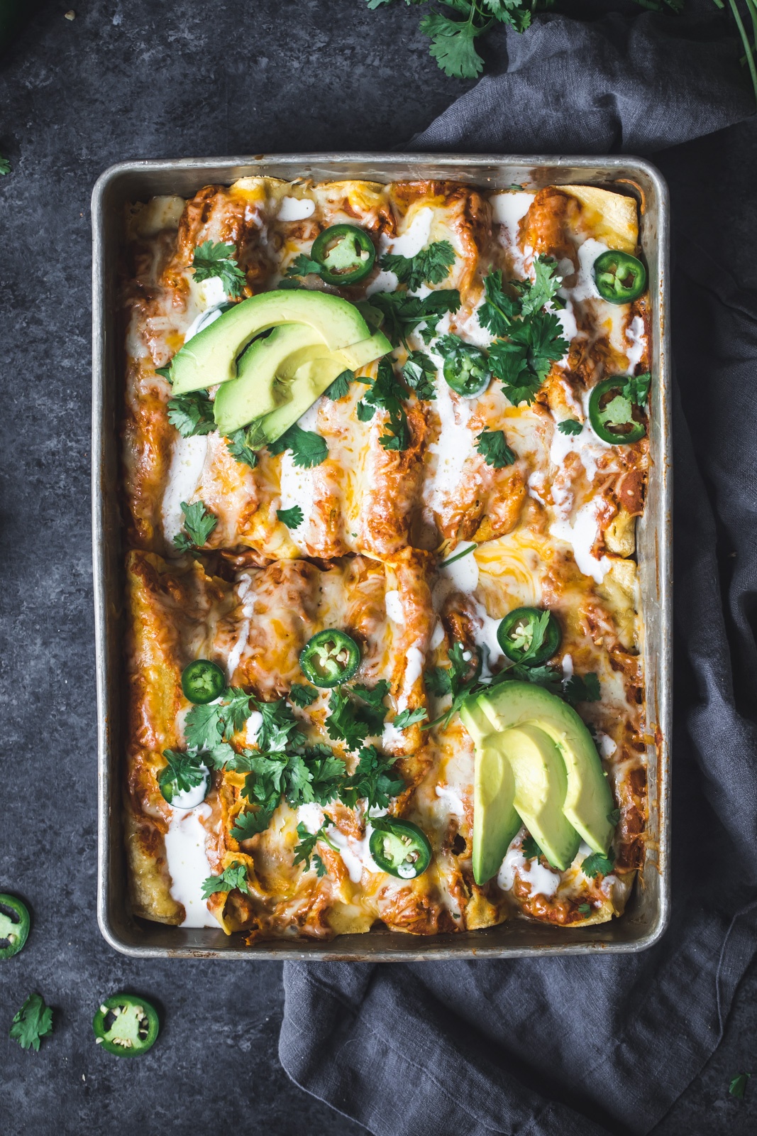 black bean chicken pumpkin enchiladas in a pan topped with avocado and jalapeño slices