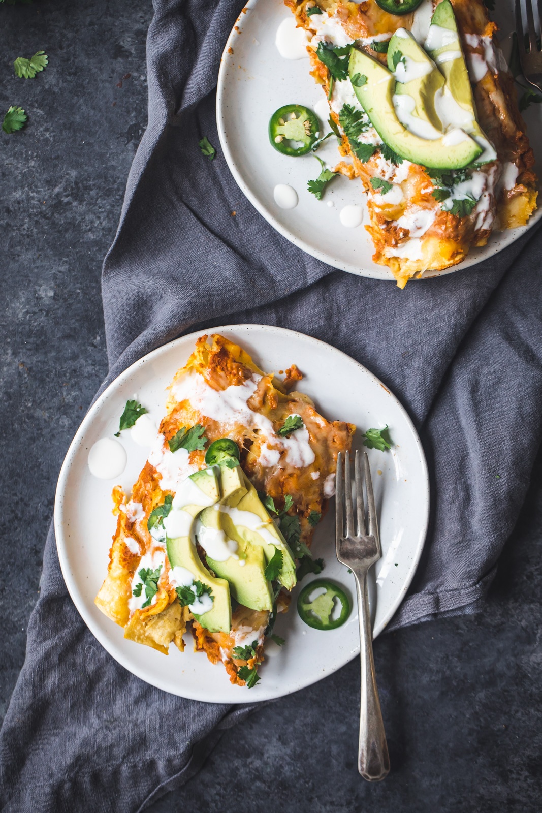 chicken pumpkin enchiladas on two plates topped with avocado