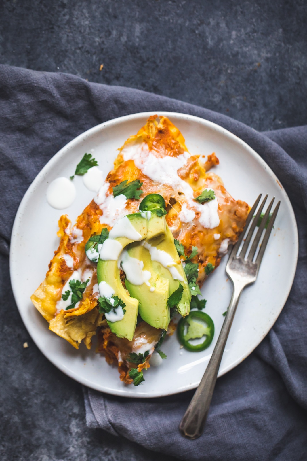 chicken pumpkin enchiladas on a plate with a fork topped with avocado 