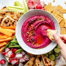 dipping pita bread into beet hummus