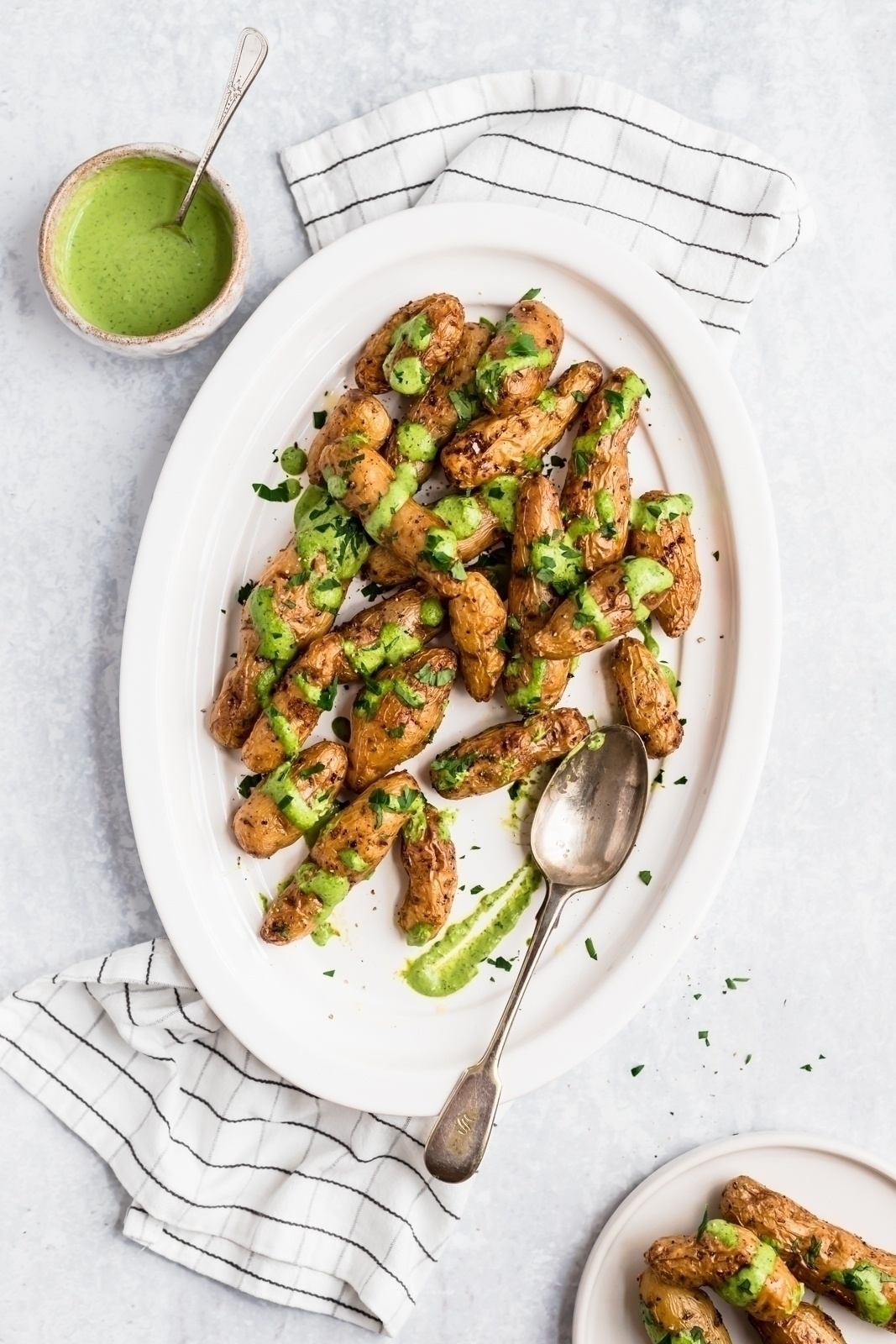 roasted garlic fingerling potatoes on a platter with green sauce drizzled on top and a spoon on the side