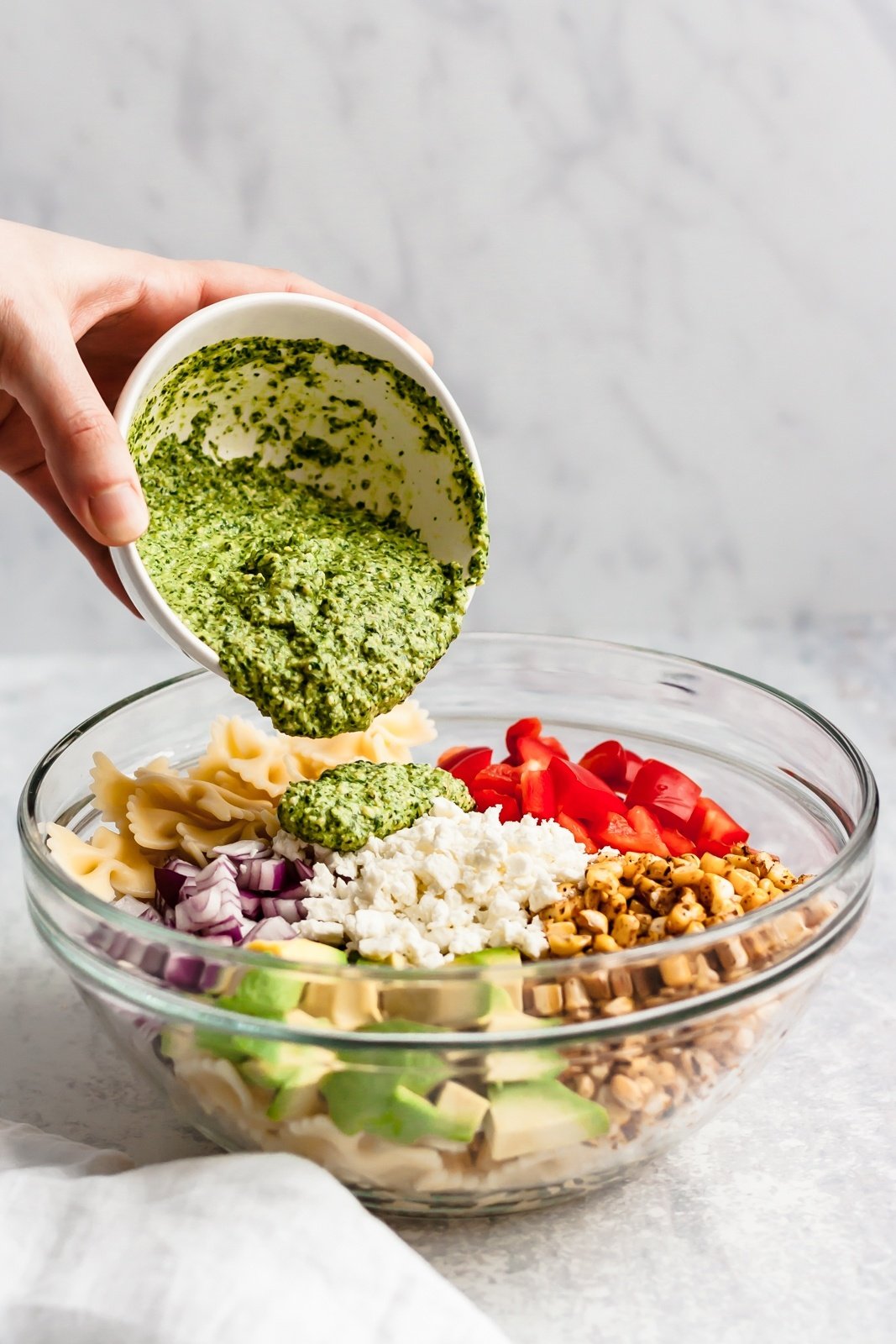 cilantro pesto being added to healthy street corn pasta salad in a bowl