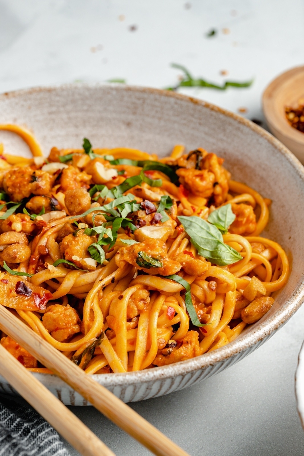 sweet and spicy chicken noodles in a bowl topped with peanuts and basil