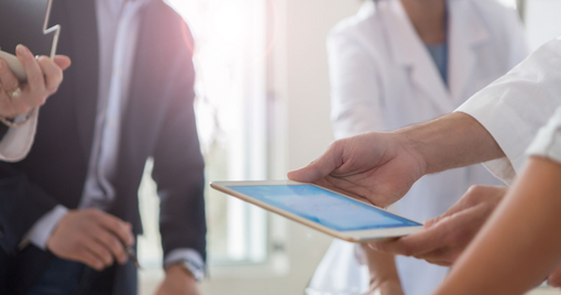 doctor uses a digital tablet while meeting with hospital management.