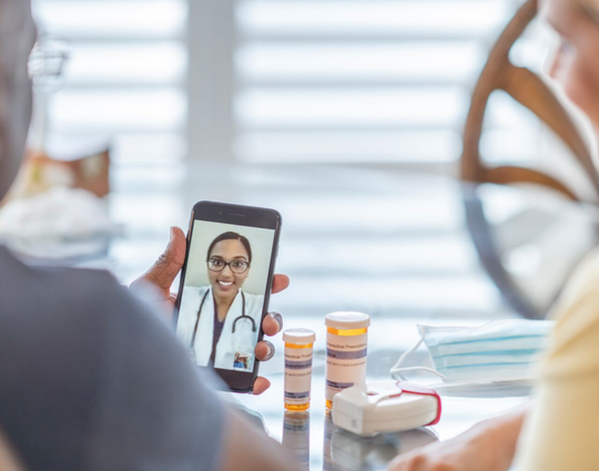 Remote medical visit between a patient and spouse and their female doctor from the patients point of view while they sit at their kitchen table.