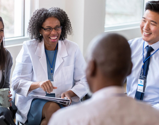 A group of cheerful medical coworkers sit in a circle for a staff meeting. 