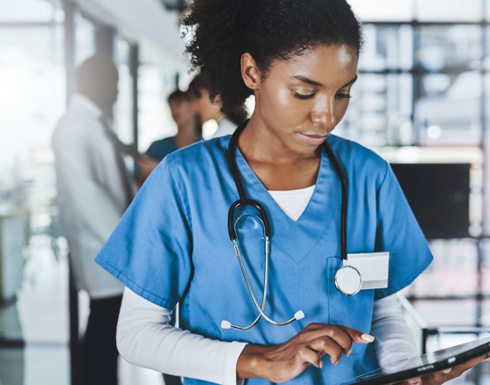 Shot of a young doctor using a digital tablet in a hospital with her colleagues in the background
